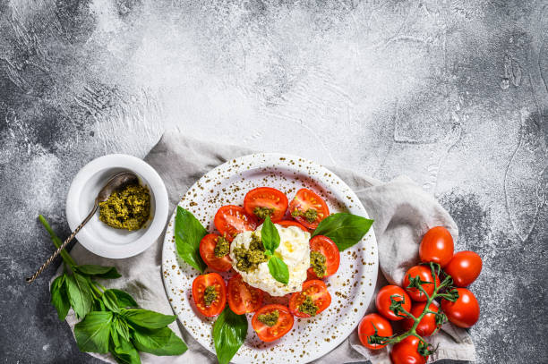istock Italian cheese stracciatella (burrata) on small plate served with fresh tomatoes and basil. Gray background. Space for text 1216823321