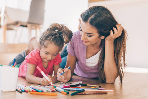 Mother and daughter coloring on the floor Young woman and a little girl with colorful pencils and coloring book woman lying on the floor isolated stock pictures, royalty-free photos & images