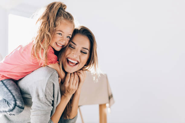 Happy mom carrying her little daughter Happy mother and daughter playing and embracing at home on shoulders stock pictures, royalty-free photos & images