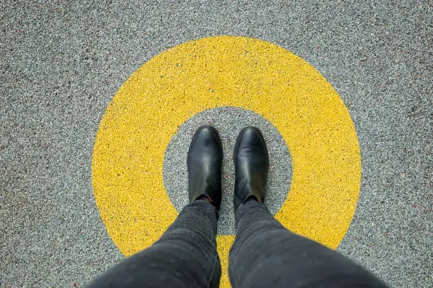 Photo of Black shoes standing in yellow circle on the asphalt concrete floor. Comfort zone or frame concept. Feet standing inside comfort zone circle