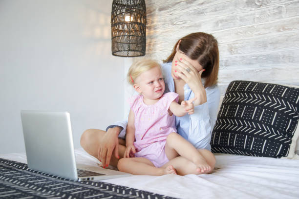 istock Work from home with a little one. Young mother trying to work on laptop while babysitting. Stressful mum trying to multitask. 1216829229