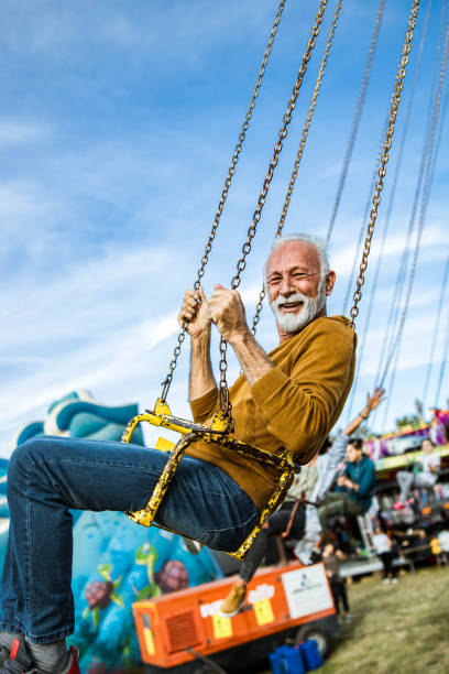 istock Happy senior man having fun while riding on chain swing at amusement park. 1216832189