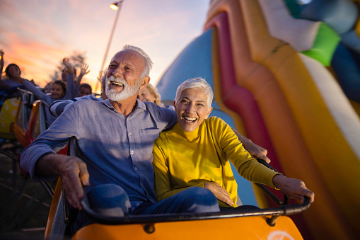 Happy senior couple having fun while riding on rollercoaster at amusement park.