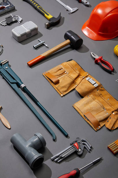 istock high angle view of tool belt, hammers, monkey wrench, putty knife, pliers, helmet, pipe connector, calipers, angle keys and brush on grey background 1216833884