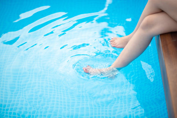 une femme a trempé ses pieds dans la piscine d’eau de sa maison. - deck chair photos et images de collection