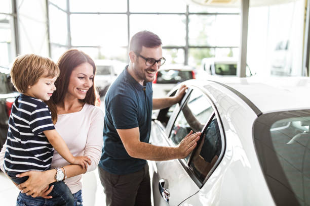 Happy family choosing a new car in a showroom. Young happy family enjoying while buying a new car in a showroom. car dealership stock pictures, royalty-free photos & images