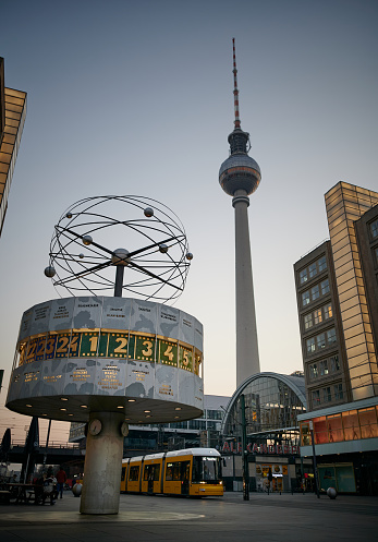 Berlin, Germany - March 27, 2020: The famous place the Berlin Alexanderplatz during dusk. A tram passing by close to the World Clock (Weltzeituhr). In the background the big television tower. Due to the lockdown because of the Coronavirus, this square is almost deserted.