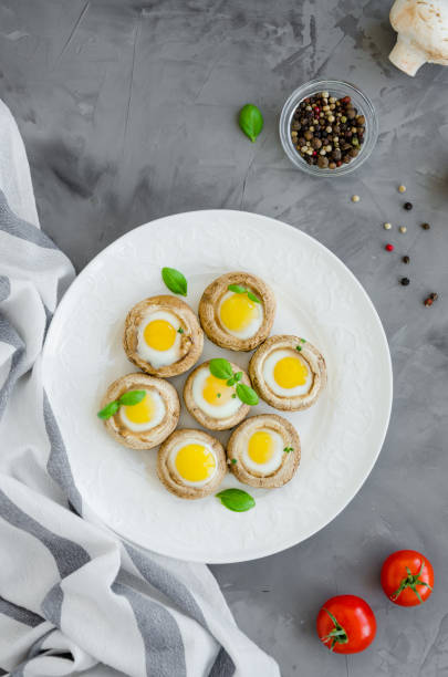istock Stuffed mushrooms with quail eggs on a white plate with basil and thyme leaves on a dark concrete background. Easter appetizer. Vertical orientation. Top view. 1216840496