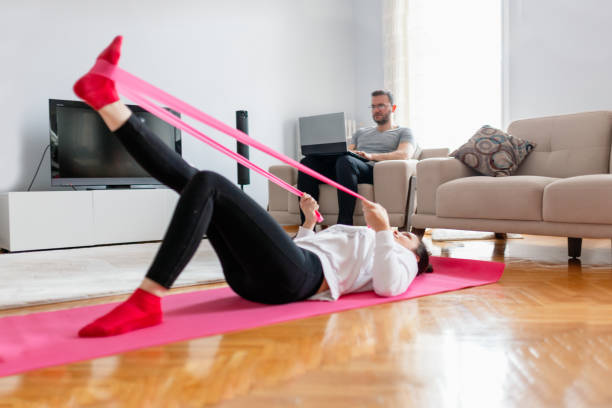 man working from home while his wife is exercising at home - the splits ethnic women exercising imagens e fotografias de stock