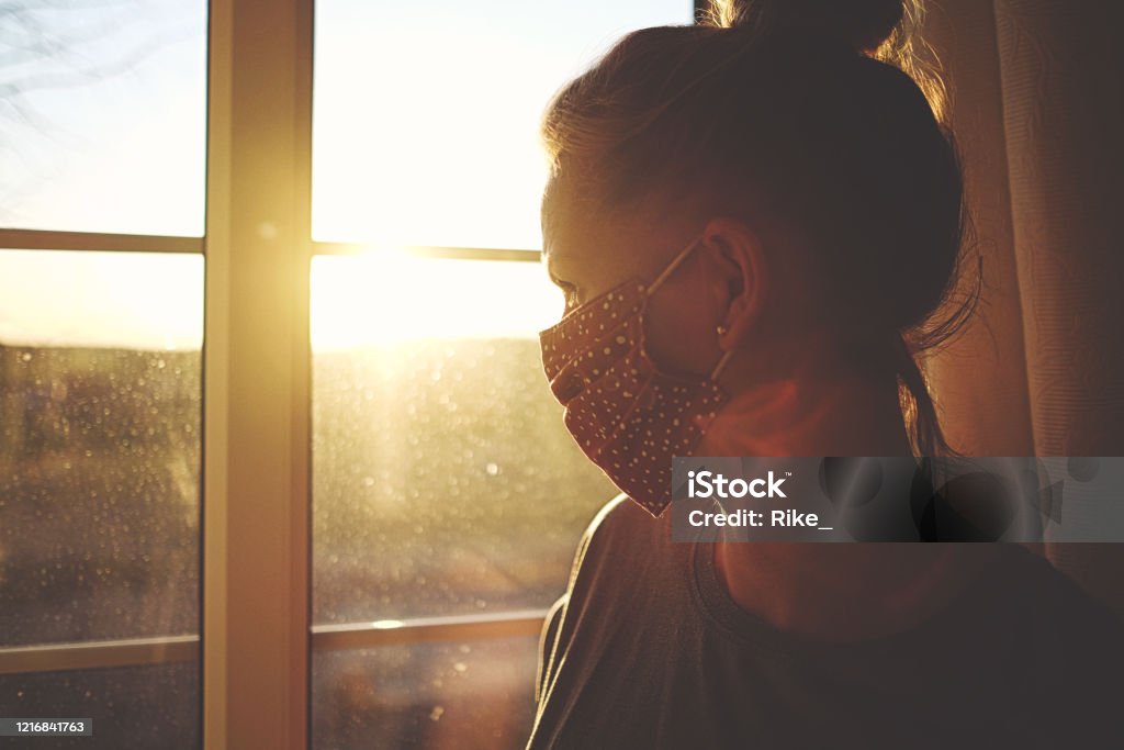 Pretty woman in quarantine with mask, looks out the window Lockdown Stock Photo