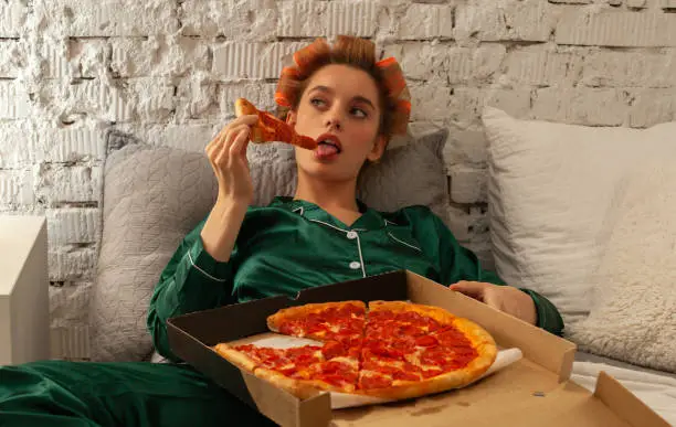 young fashionable lonely woman in pajama with pizza box in bed at home, self-isolation issue