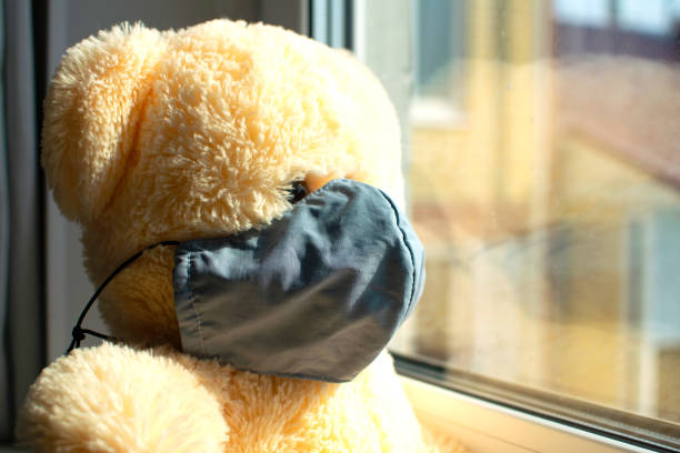 istock Teddy bear in a medical protective mask on window. 1216848025