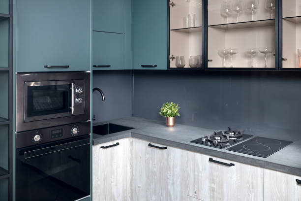 istock Upscale Aqua Menthe kitchen in luxury home with hob induction electric microwave oven flat wooden panels design. 1216851322
