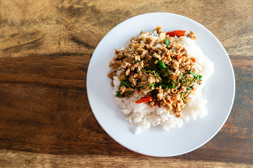 Rice topped with stir-fried pork and basil in a white dish.