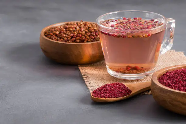 Sumac water or tea and dried ground red Sumac spices in wooden spoon with sumac berries on rustic table. Healthy food concept