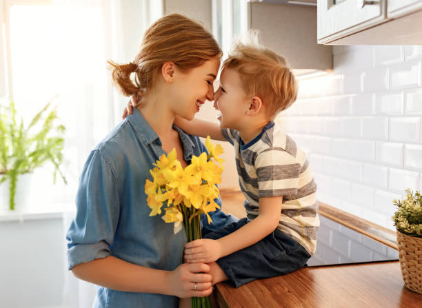 kleiner sohn gratuliert mutter in der küche - people care surprise love stock-fotos und bilder