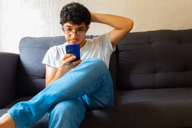 young hispanic man using smartphone on a sofa