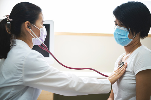 Asian female doctor wearing medical mask using stethoscope checking patient lung for check Pneumonia or coronavirus at hospital.