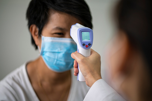 Female doctor check Asian woman body temperature using infrared forehead thermometer (thermometer gun) for virus symptom at hospital.