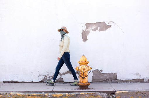 A woman walking down a sidewalk wearing a bandana mask against COVID-19. Shot in Santa Fe, NM.