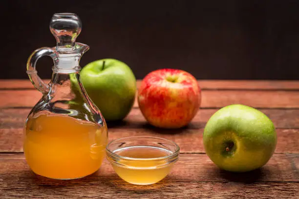 unfiltered, raw apple cider vinegar with mother - a cruet with a small glass  bowl surrounded by fresh  apples on rustic wood