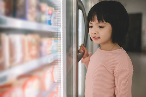 an asian chinese young girl holding a refrigerator door knob at the refrigerated section in supermarket an asian chinese young girl holding a refrigerator door knob at the refrigerated section in supermarket refrigerated section supermarket photos stock pictures, royalty-free photos & images
