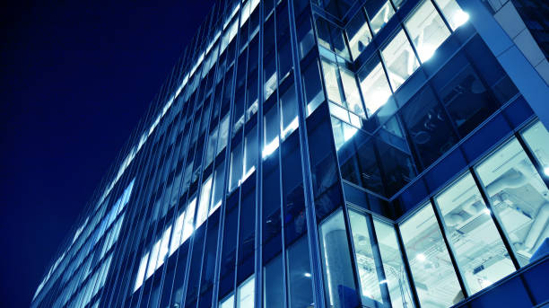 istock Pattern of office buildings windows illuminated at night. Lighting with Glass architecture facade design with reflection in urban city. 1216902150