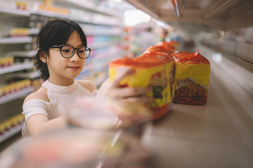 an asian chinese young girl selecting goods item from the shelf and picking up one of them in supermarket