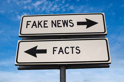 Fake news vs facts. White two street signs with arrow on metal pole with word. Directional road. Crossroads Road Sign, Two Arrow. Blue sky background. Two way road sign with text.