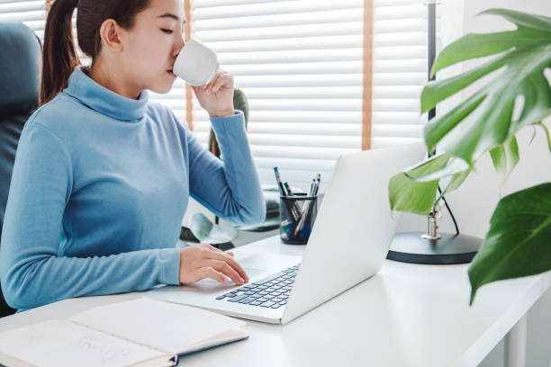 istock Asian woman working from home using computer and drinking coffee in her bedroom document finance and conference online meeting for new projects 1216908290