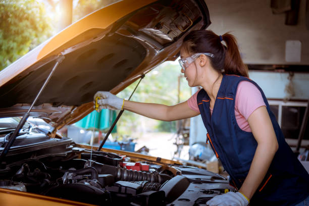 a woman car mechanic repairing car with open hood view and checking level motor oil for refill or clean in car garage service - vehicle breakdown hood car oil change imagens e fotografias de stock