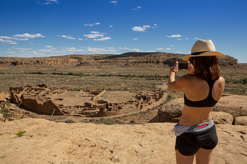 Woman taking a cell phone photograph from the hiking trail cliffs of Pueblo Bonito at Chaco Canyon Historical National Monument, New Mexico