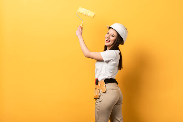 istock smiling handywoman holding paint roller on yellow background with copy space 1216911729