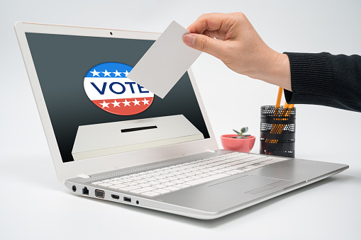 Online vote concept. Online voting concept with a man with a ballot in hand putting a ballot toward the computer monitor.