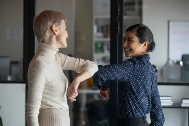 Photo of Friendly smiling millennial diverse female colleagues keeping social distance.