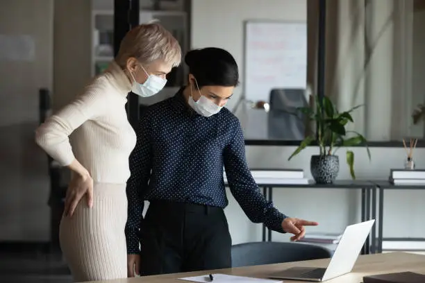 Photo of Focused two women in medical protective masks working in office.