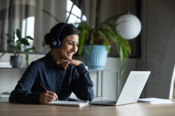 feliz joven chica india con auriculares mirando la pantalla del ordenador portátil. - lecture notes fotografías e imágenes de stock