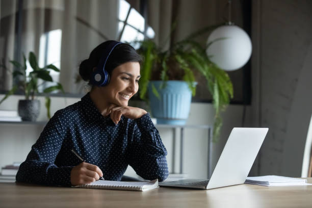 happy young indian girl with headphones looking at laptop screen. - cyber imagens e fotografias de stock