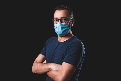 Adult person with protective face mask posing on a black background - social issues with virus and hygiene safety measures.