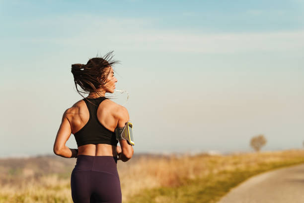 vista trasera de la mujer de construcción muscular corriendo en la naturaleza. - sostén deportivo fotografías e imágenes de stock