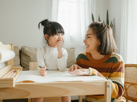 Cute and lovely asian little girl doing homework at home, with a help of her mother.