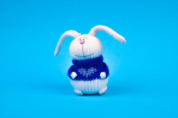 istock White knitted rabbit, in a blue jacket with a heart, on a blue background. Rabbit with a heart. place for writing 1216921522
