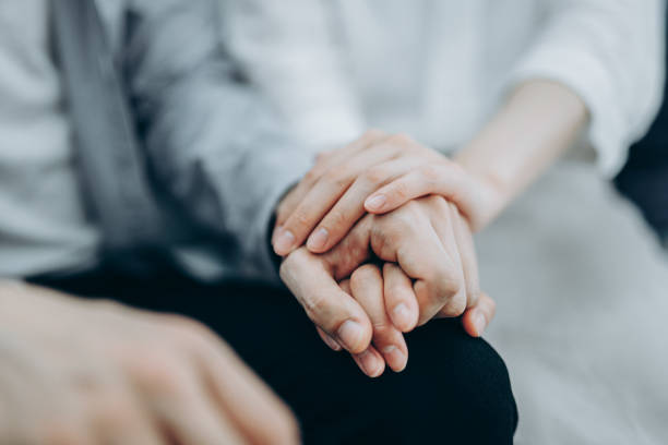 cropped shot of a young couple sitting on sofa compassionately holding hands in self isolation during covid-19 health crisis - holding hands human hand romance support imagens e fotografias de stock