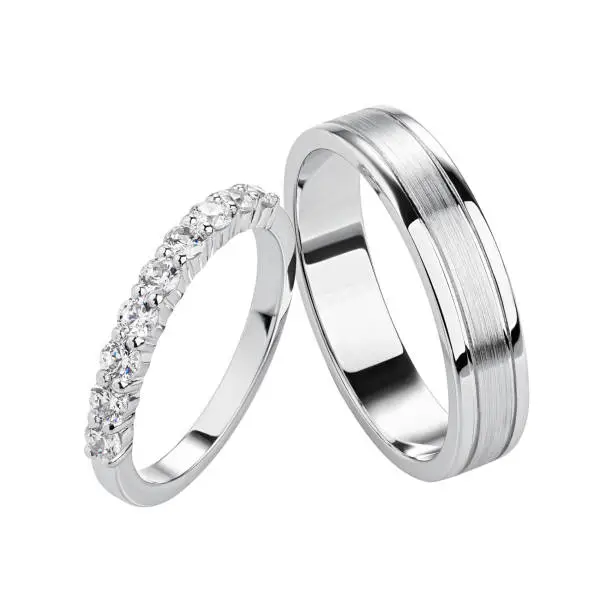 Pair of silver wedding rings isolated on white background. White gold ring bands with diamonds on female ring and matte textured surface on male ring