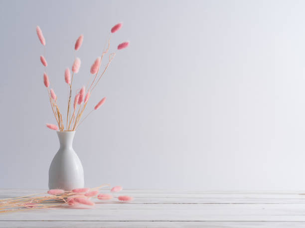 Pink bunny tail grass in vase on a white wooden table.
