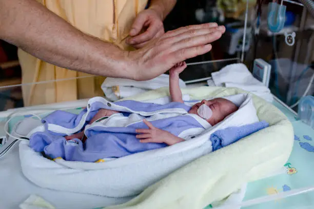 premature baby lies in the heat bed and gives high five to his Dad