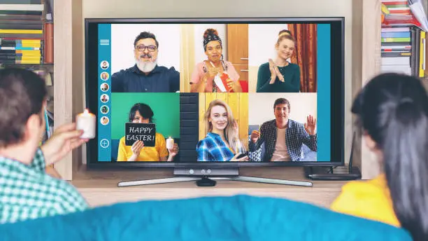Photo of Multicultural friends at home isolation celebrating Easter holiday online streaming live on video call while holding candles and having fun in quarantine keeping social distance