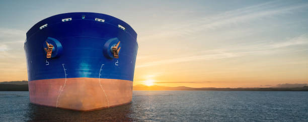 Close up of large blue merchant crago ship in the ocean underway. at sunrise or sunset .Performing cargo export and import operations. Close up of large blue merchant crago ship in the ocean underway at sunrise or sunset. Performing cargo export and import operations with sun rays, horizon line and beautiful sky. bulk carrier stock pictures, royalty-free photos & images