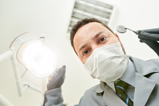 Close-up of a male dentist wearing surgical mask looking at a patient