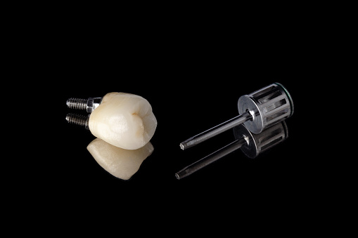 ceramic tooth on the implant with pronounced anatomy and a metal screwdriver for twisting the crown to the implant. isolated on a black background. orthopedic dentistry. dental implantation concept